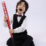 A young boy in a suit and a KIKI and JOJO Kids Bow Tie – Burgundy Bear – Pre-Tied Satin – Adjustable sits on the floor, smiling widely while holding a red baseball bat with "Supreme" printed on it.