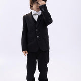 A young boy wearing a KIKI and JOJO Kids Bow Tie – White & Black – Pre-Tied Satin – Adjustable stands against a plain background, covering his eyes with one hand.