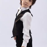 A young boy from KIKI and JOJO wears the Kids Bow Tie – White & Black – Pre-Tied Satin – Adjustable, standing slightly turned and looking at the camera against a plain light background.