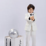 A young boy in a classic KIKI and JOJO Kids Bow Tie – White & Black – Pre-Tied Satin with adjustable fit smiles while popping a party popper, celebrating in style next to a gift bag with a silver balloon inside.