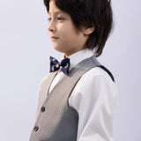 A young boy with dark hair wears a white shirt, grey vest, and the KIKI and JOJO Kids Bow Tie – Navy Blue Bear – Pre-Tied Satin – Adjustable, standing in profile against a plain light background.