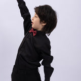 A young boy in a black shirt and KIKI and JOJO’s Kids Bow Tie – Burgundy & Black holds a red baseball bat above his head, highlighting this stylish pre-tied satin bow tie’s premium quality and adjustable fit.