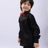A young boy wears the KIKI and JOJO Kids Bow Tie – Burgundy & Black – Pre-Tied Satin Adjustable, paired with a black dress shirt and pants, standing against a light background and smiling at the camera.