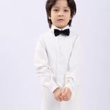 A young boy models the KIKI and JOJO Kids Bow Tie – Black with White Dots, a pre-tied satin bow tie with an adjustable fit, standing against a plain white background and looking at the camera with a neutral expression.