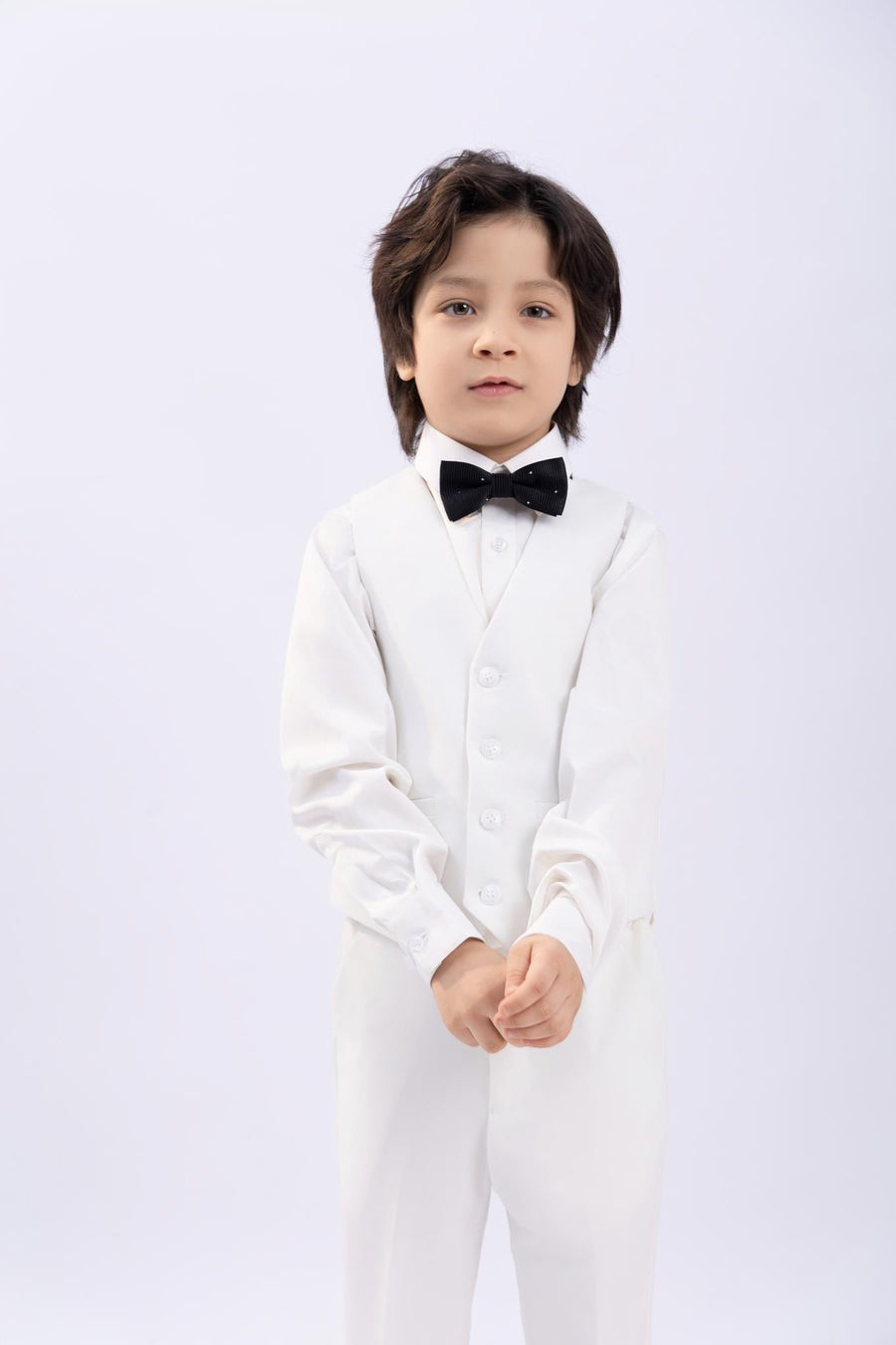 A young boy models the KIKI and JOJO Kids Bow Tie – Black with White Dots, a pre-tied satin bow tie with an adjustable fit, standing against a plain white background and looking at the camera with a neutral expression.