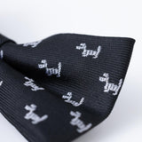 Close-up of KIKI and JOJO Kids Bow Tie – Black Puppy, a pre-tied adjustable satin bow tie in classic black, featuring a pattern of small white dog silhouettes.