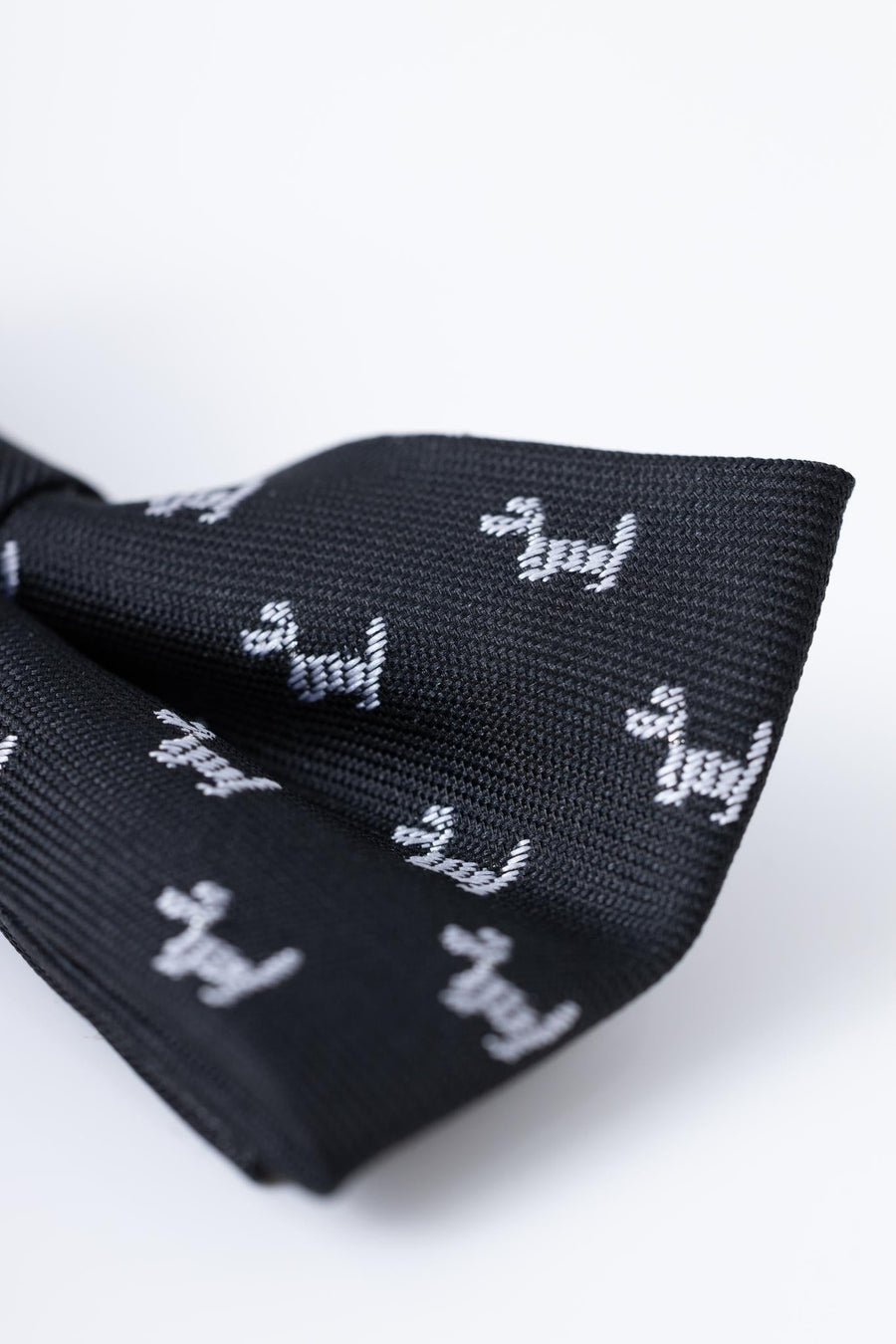 Close-up of KIKI and JOJO Kids Bow Tie – Black Puppy, a pre-tied adjustable satin bow tie in classic black, featuring a pattern of small white dog silhouettes.