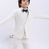 A young boy, arms outstretched against a plain light background, wears a white suit and the KIKI and JOJO Kids Bow Tie – Black Puppy – Pre-Tied Satin – Adjustable.