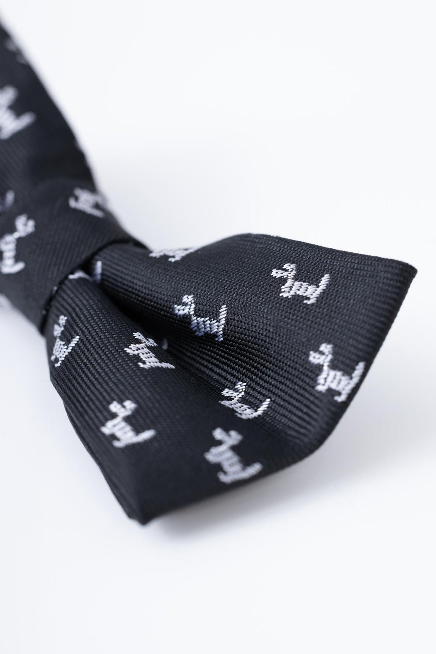 The KIKI and JOJO Kids Bow Tie – Black Puppy is a pre-tied, adjustable satin bow tie in classic black with small white embroidered dogs, offering easy and stylish wear for children.