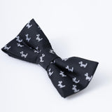 The KIKI and JOJO Kids Bow Tie in black features a playful white puppy pattern. This pre-tied, satin bow tie is adjustable for comfort and is displayed on a plain white background.