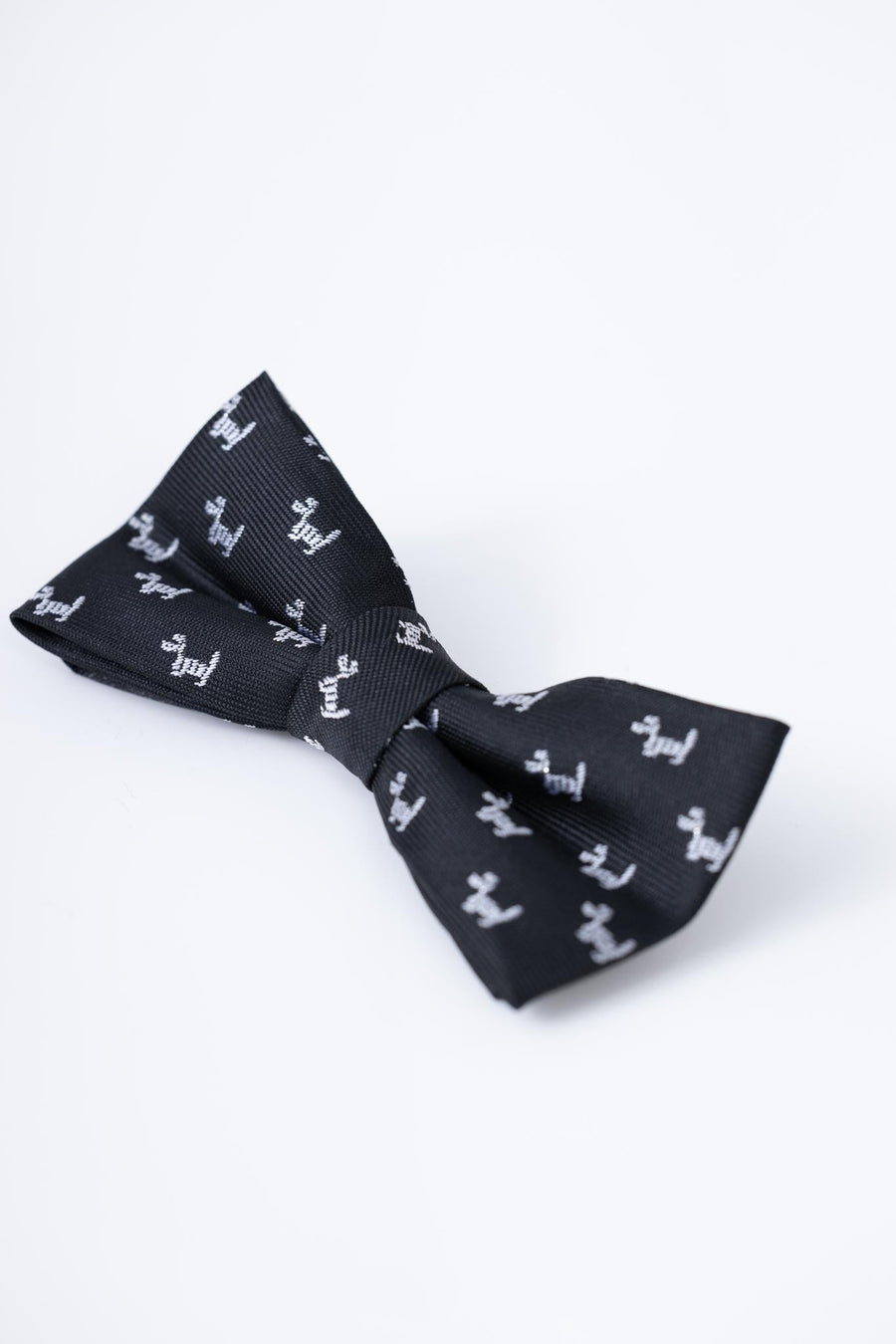 The KIKI and JOJO Kids Bow Tie in black features a playful white puppy pattern. This pre-tied, satin bow tie is adjustable for comfort and is displayed on a plain white background.