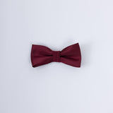 The KIKI and JOJO Kids Bow Tie – Pre-Tied Burgundy Satin – Adjustable is shown against a light gray background, making it a stylish choice for any special occasion.