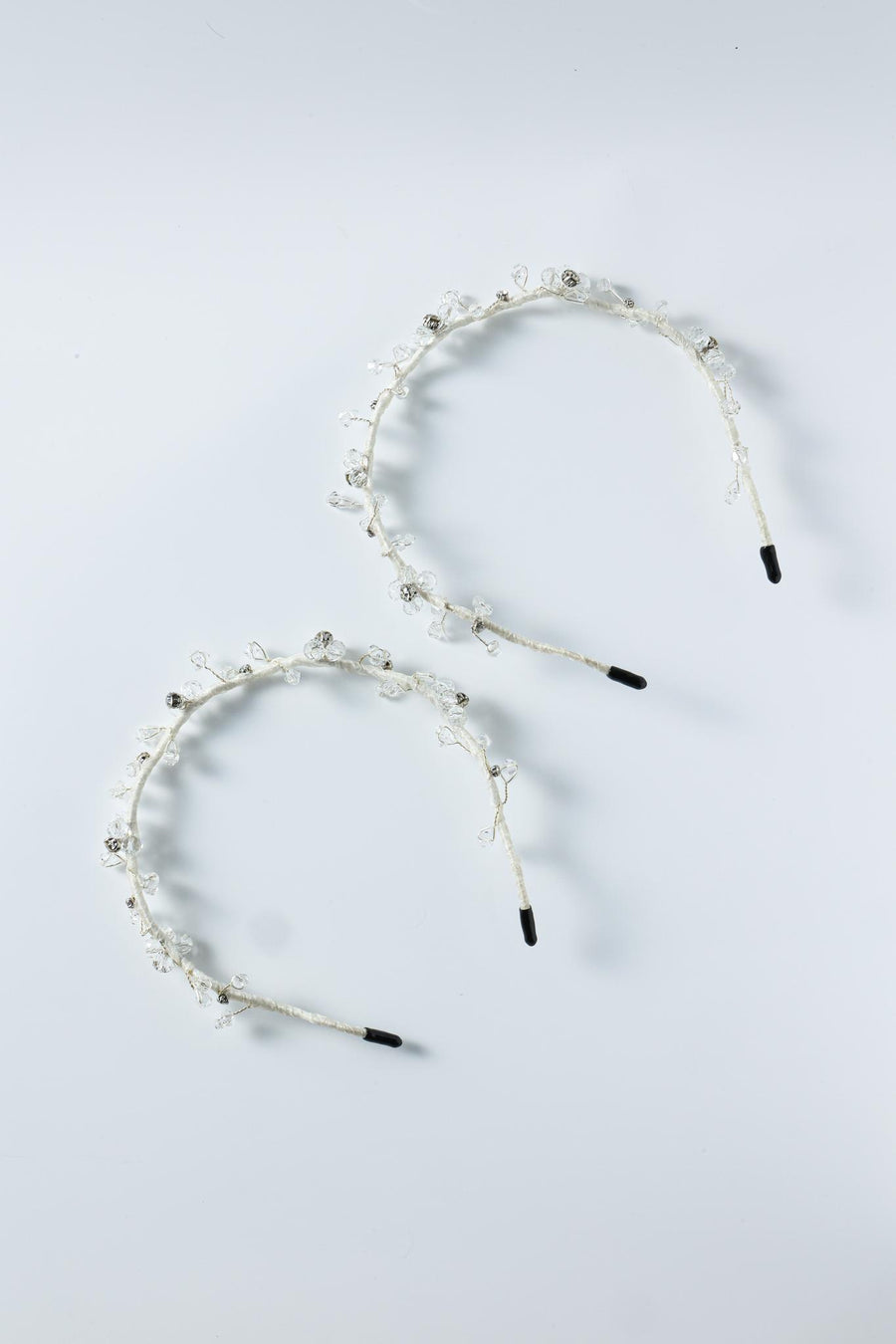 Two KIKI and JOJO Beaded Flower Girl Headbands – Gold Wire-Wrapped, adorned with small beaded flowers and black-tipped wire loops, are arranged side by side on a light gray surface.