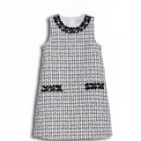 KIKI and JOJO’s Girls Tweed Dress in black & white checkered pearl features a sleeveless design, two front pockets, and a pearl-adorned neckline—ideal for special occasions, shown on a white background.
