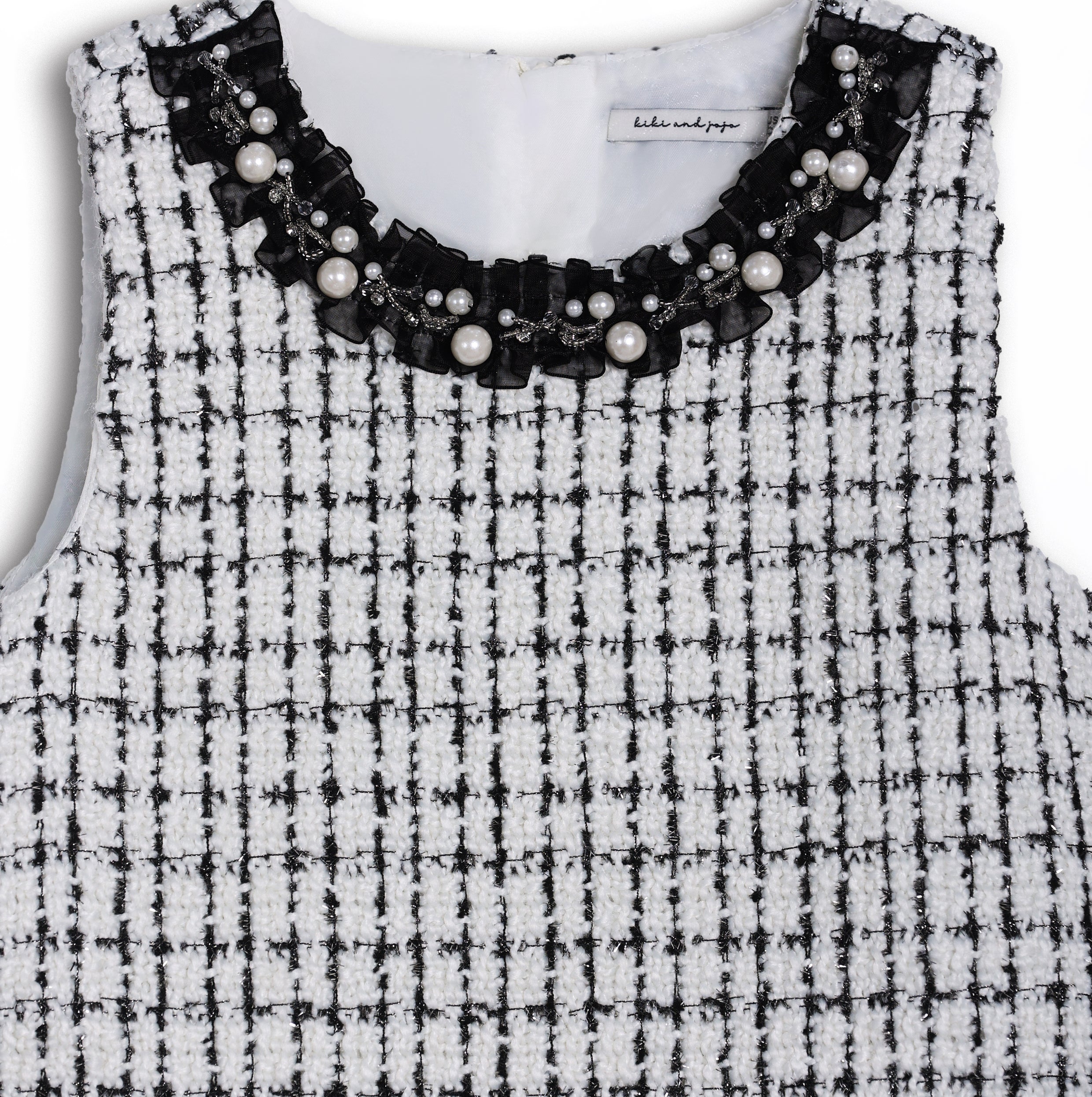 The KIKI and JOJO Girls Tweed Dress – Black & White Checkered Pearl features a sleeveless design, round neckline adorned with pearls and beads, and a classic check pattern—ideal for special occasions.