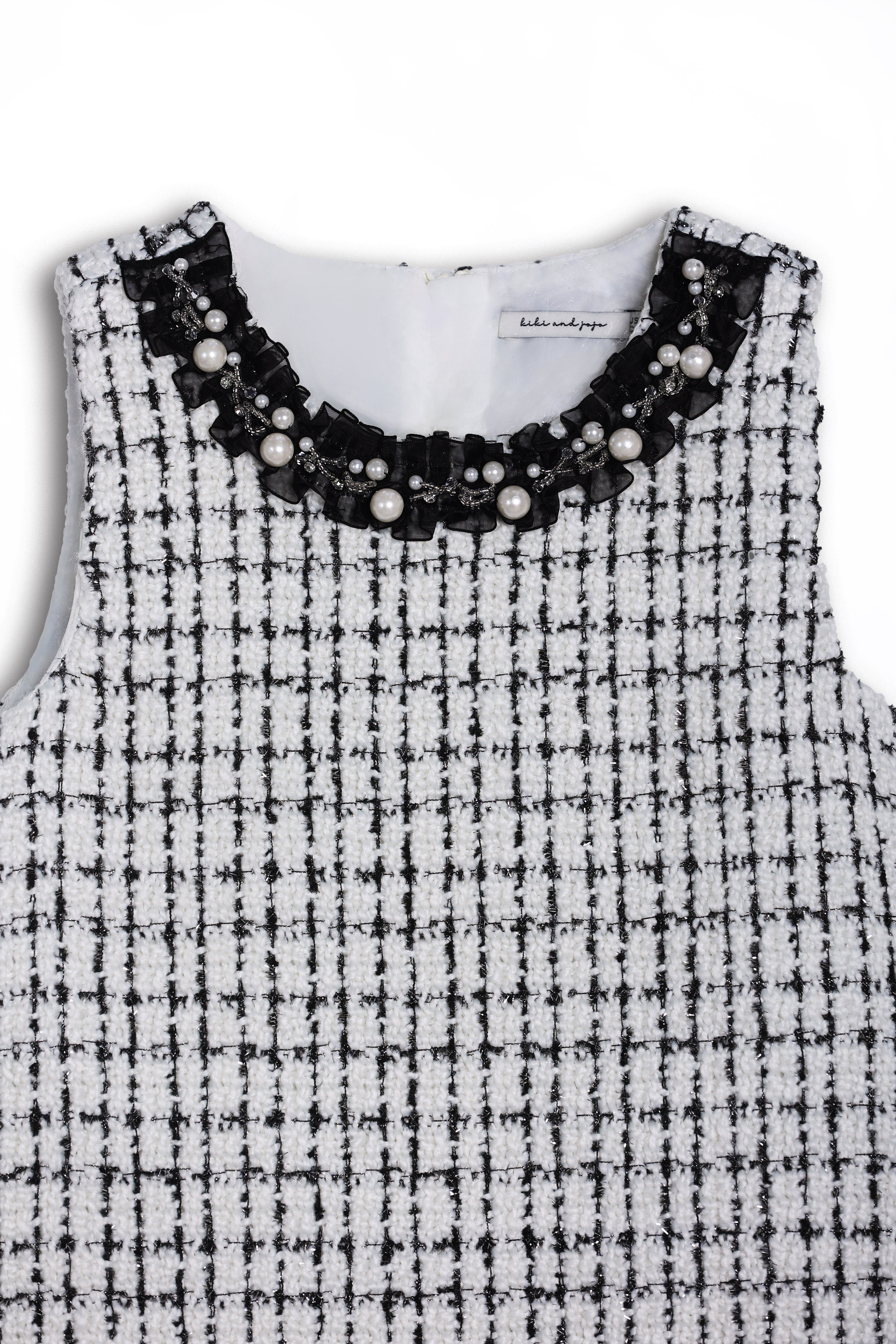 The KIKI and JOJO Girls Tweed Dress – Black & White Checkered Pearl features a sleeveless design, round neckline adorned with pearls and beads, and a classic check pattern—ideal for special occasions.