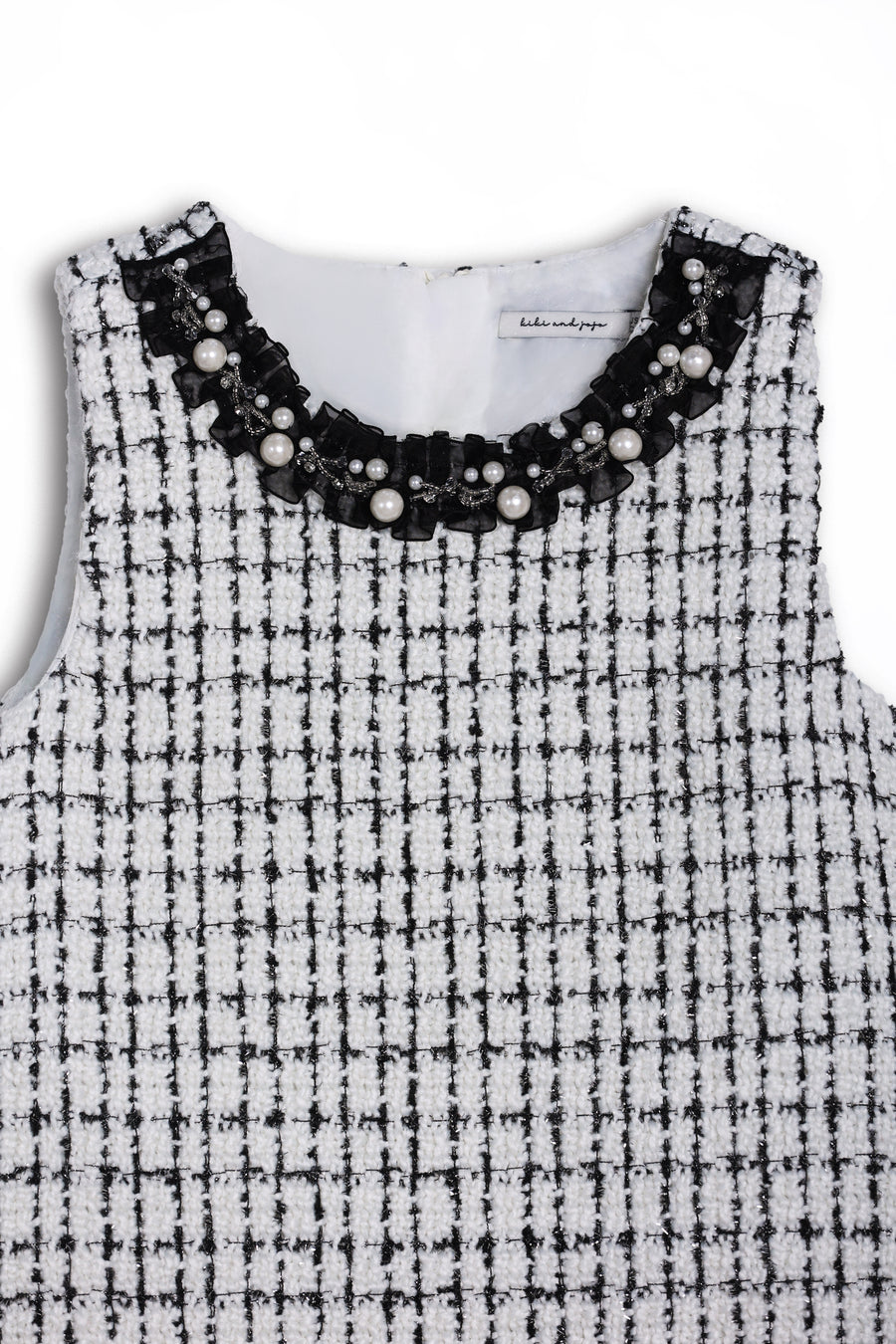 The KIKI and JOJO Girls Tweed Dress – Black & White Checkered Pearl features a sleeveless design, round neckline adorned with pearls and beads, and a classic check pattern—ideal for special occasions.