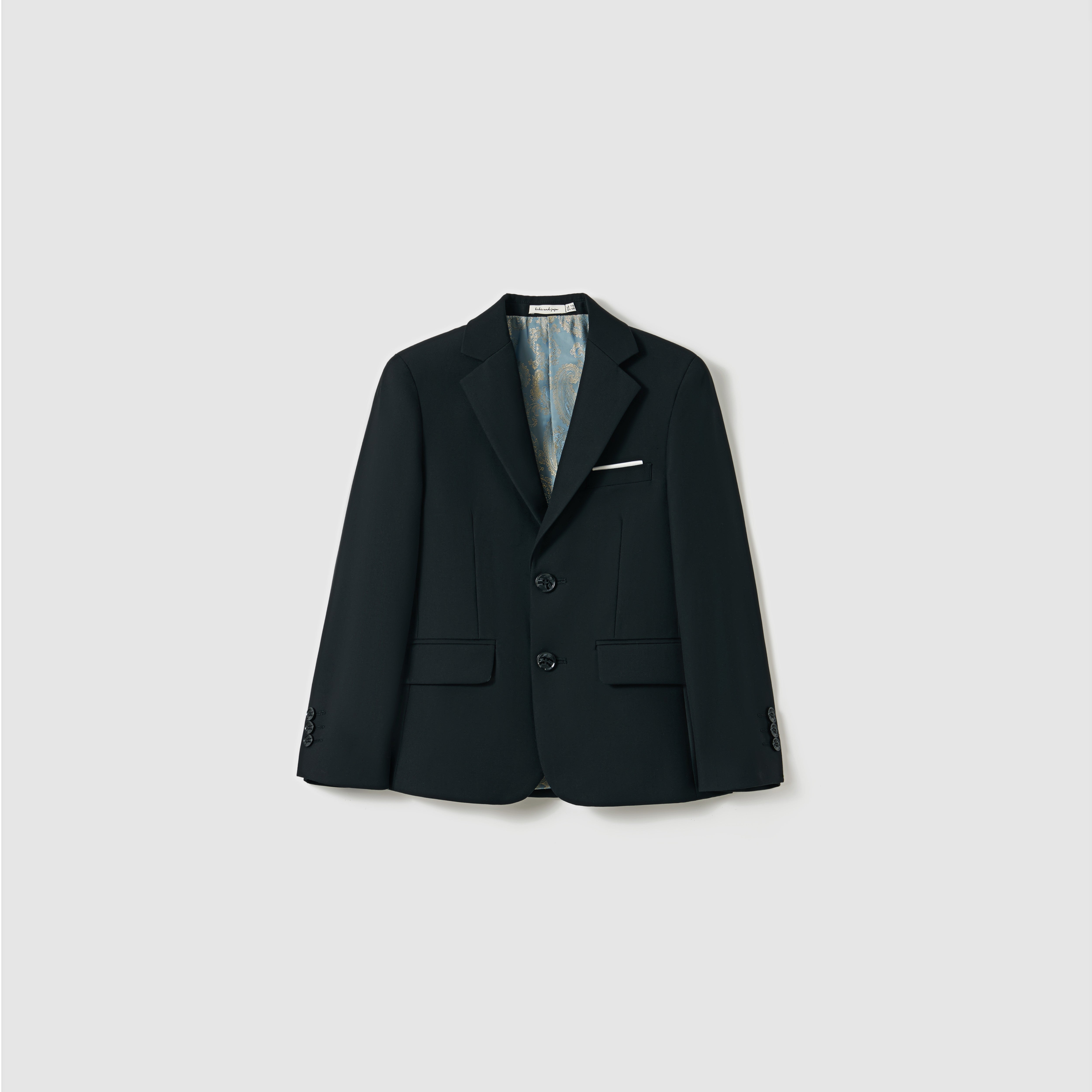 The Noir Bloom Suit Jacket by KIKI and JOJO is a boys' black suit jacket with classic notched lapels, two buttons, a white pocket square, and front flap pockets, shown on a plain light gray background.