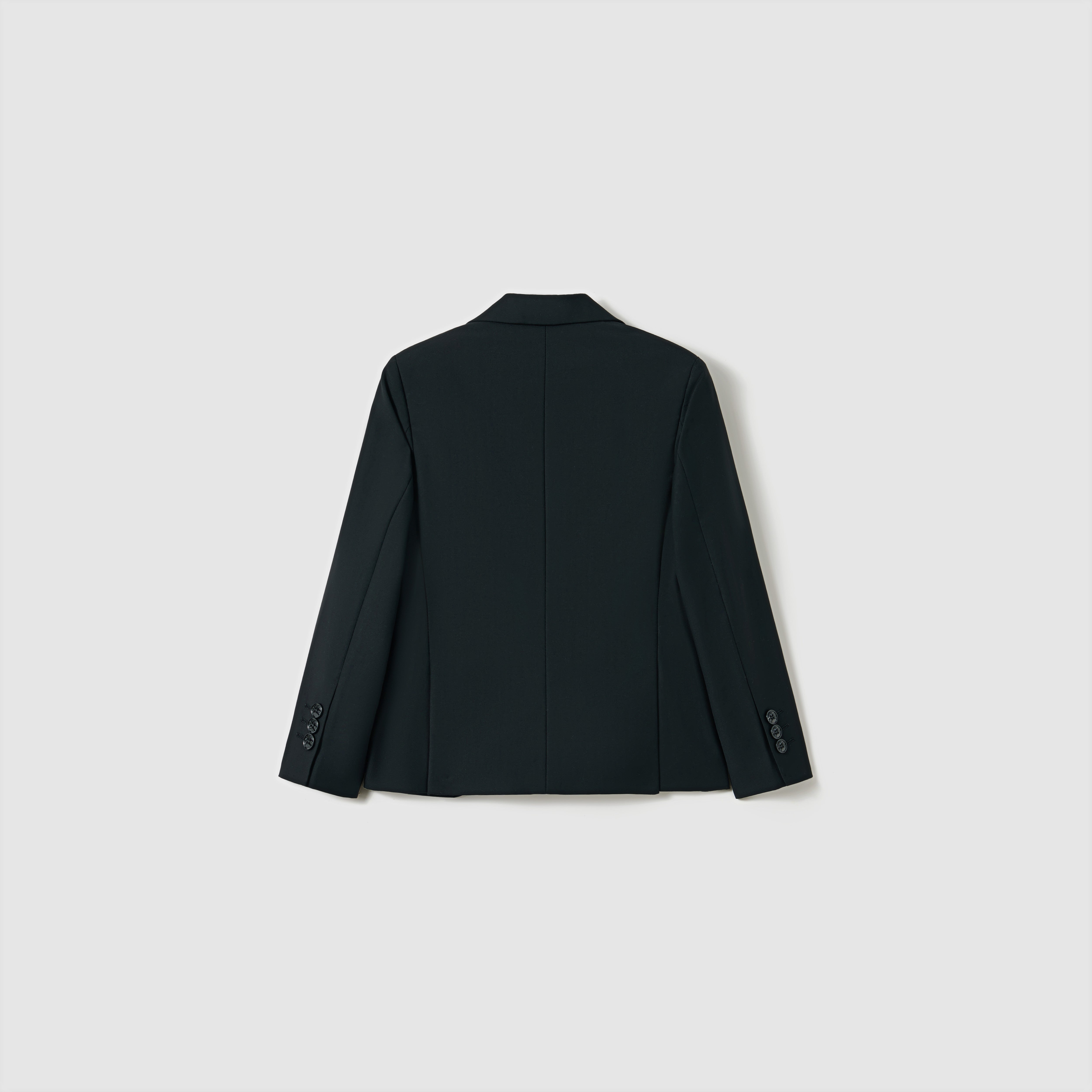The Noir Bloom Suit Jacket by KIKI and JOJO is shown from the back against a light gray background. This boys' black tailored jacket features long sleeves with buttoned cuffs and a classic notched lapel for timeless style.