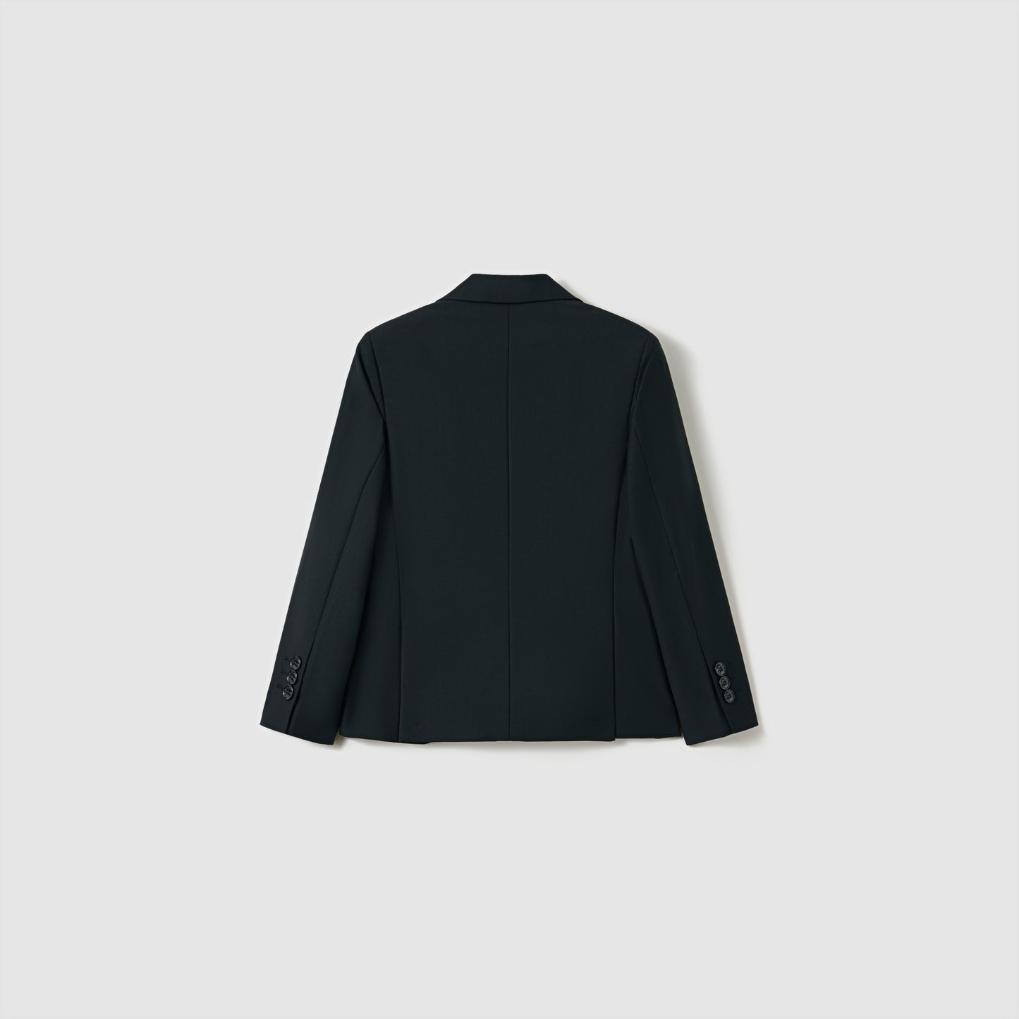 The Noir Bloom Suit Jacket by KIKI and JOJO is shown from the back against a light gray background. This boys' black tailored jacket features long sleeves with buttoned cuffs and a classic notched lapel for timeless style.