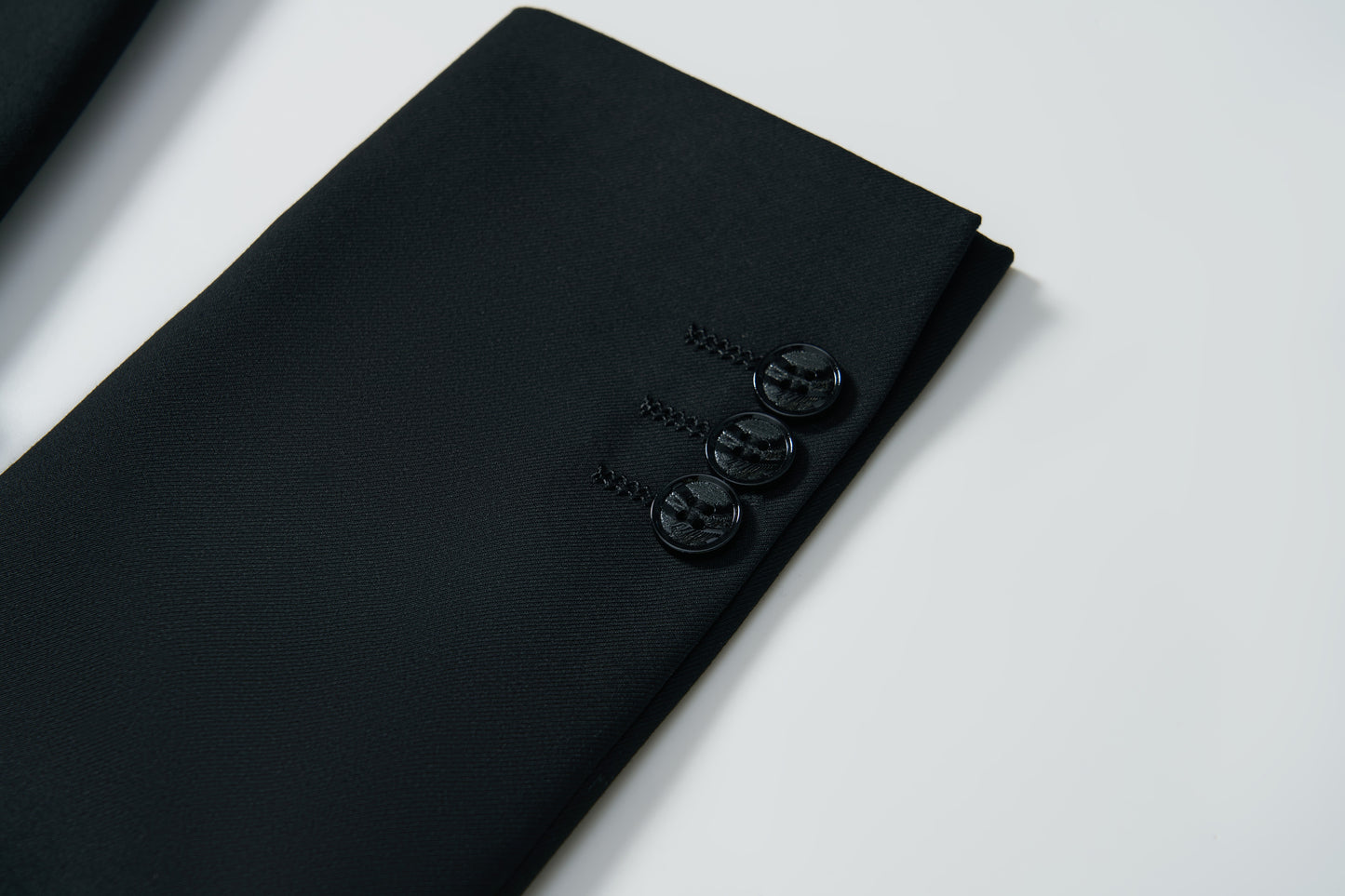 Close-up of the sleeve of the KIKI and JOJO Noir Bloom Suit Jacket for boys, showing three black buttons against a white background.