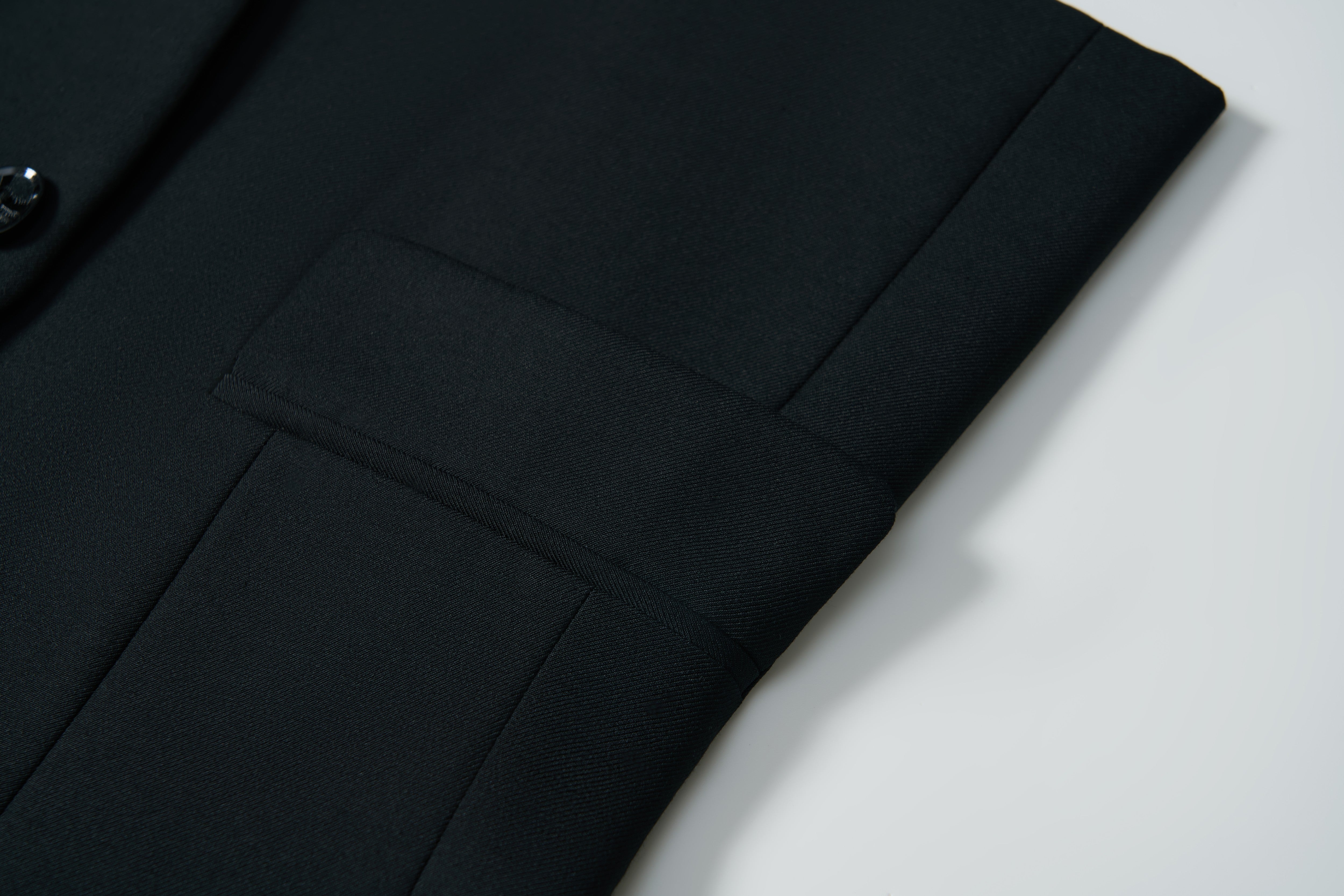 Close-up of the Noir Bloom Suit Jacket by KIKI and JOJO, featuring a neatly folded black sleeve with classic notched lapel, visible button, and seam detail displayed on a white surface.
