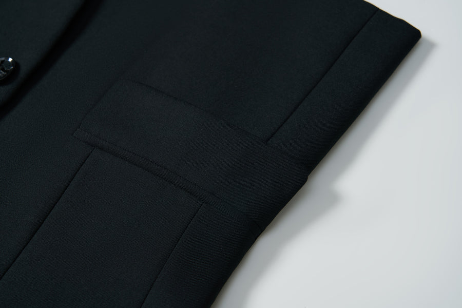 Close-up of the Noir Bloom Suit Jacket by KIKI and JOJO, featuring a neatly folded black sleeve with classic notched lapel, visible button, and seam detail displayed on a white surface.