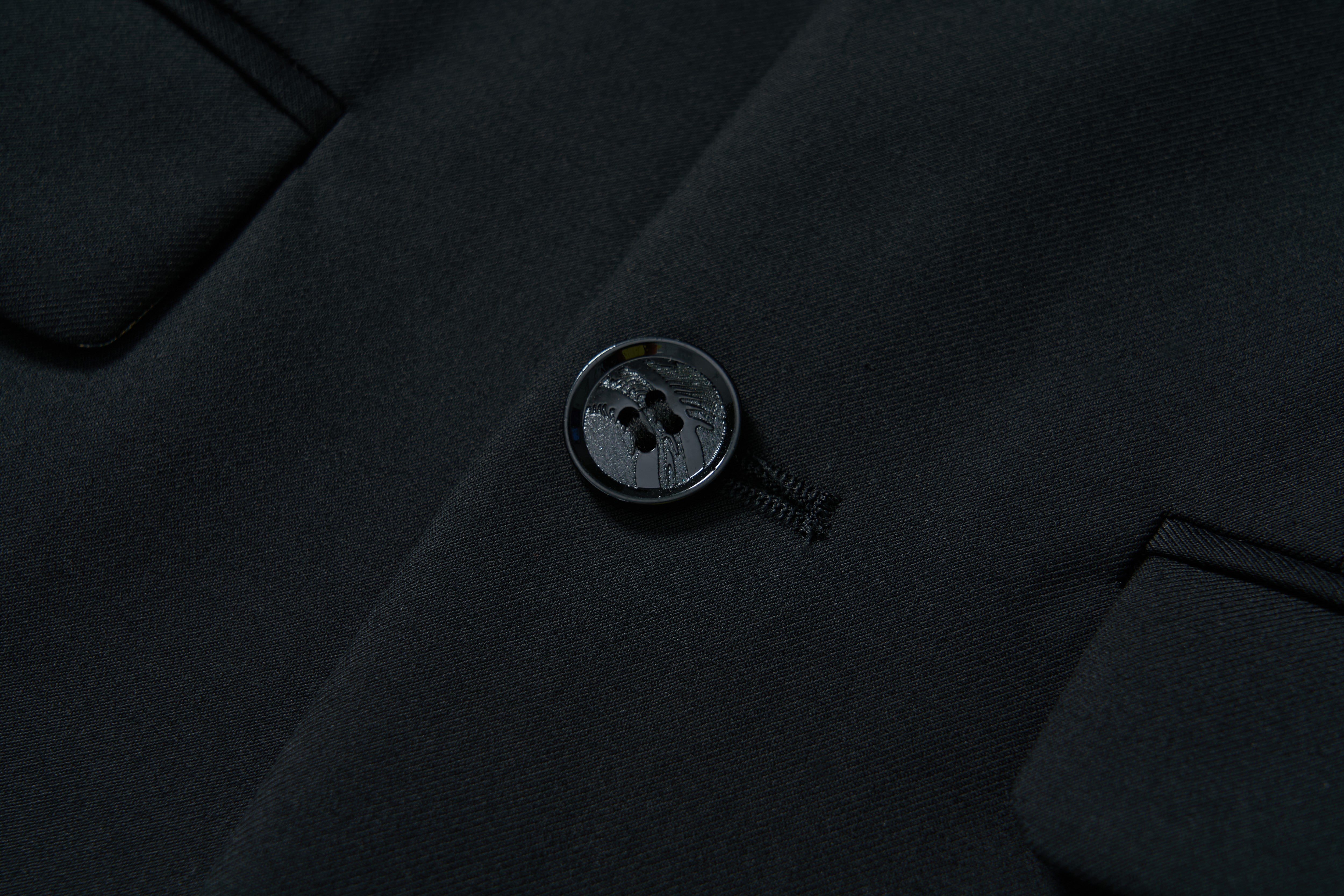 Close-up of the KIKI and JOJO Noir Bloom Suit Jacket shows a fastened button on black fabric, classic notched lapel, fine stitching, and two pocket flaps on each side.