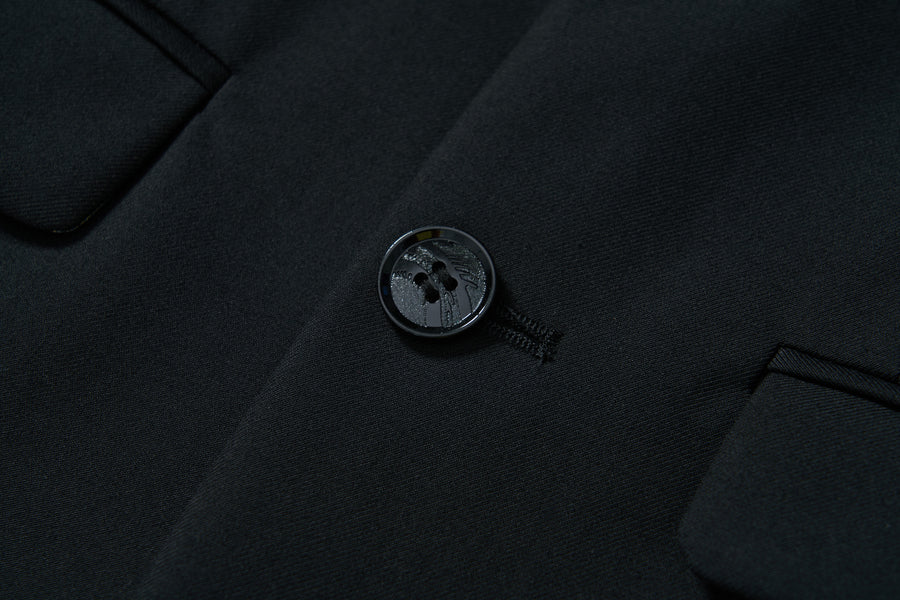 Close-up of the KIKI and JOJO Noir Bloom Suit Jacket shows a fastened button on black fabric, classic notched lapel, fine stitching, and two pocket flaps on each side.