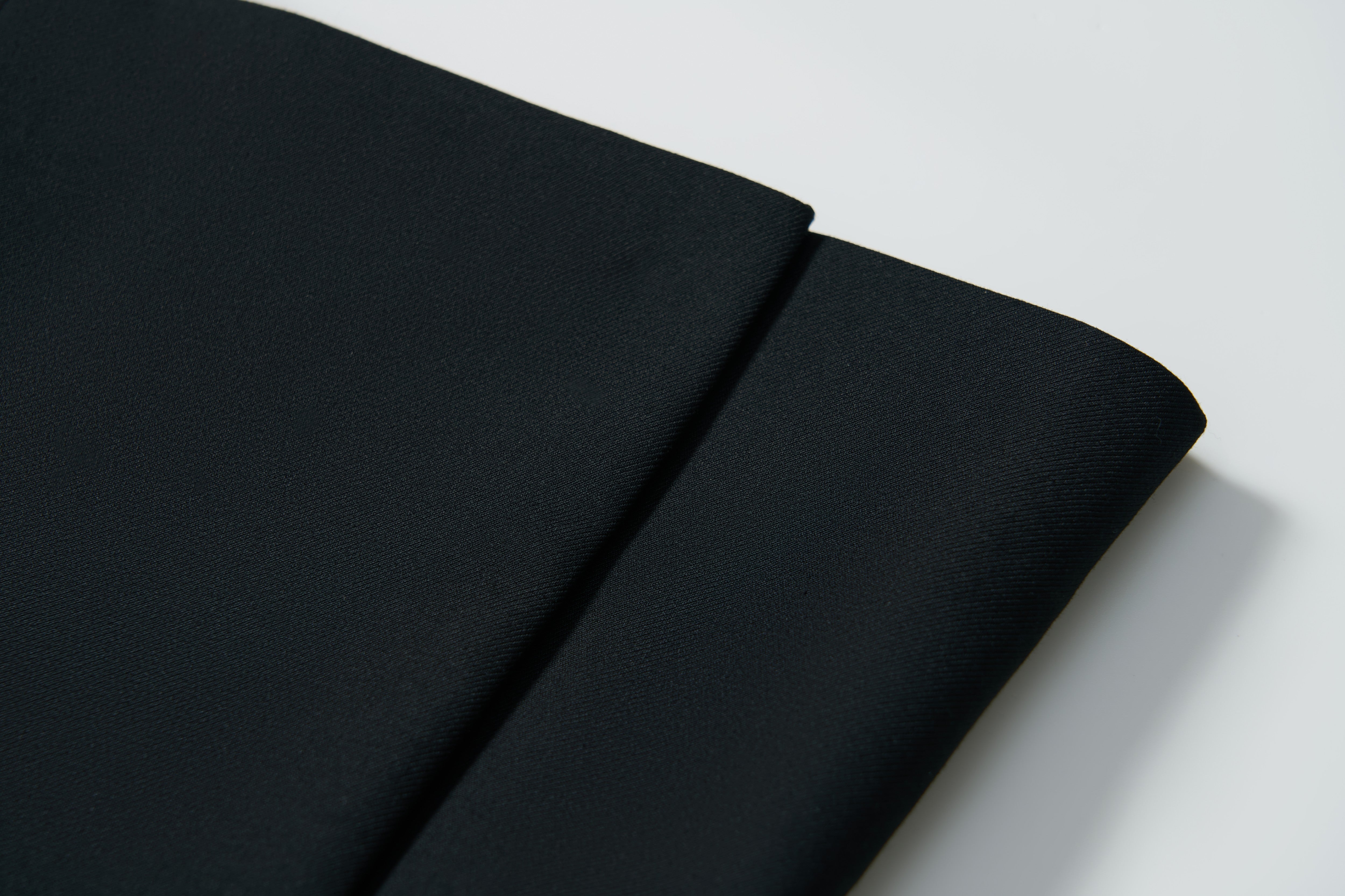 Close-up of two folded pieces of plain black fabric on a white surface—ideal for creating the KIKI and JOJO Noir Bloom Suit Jacket, a timeless choice for boys.