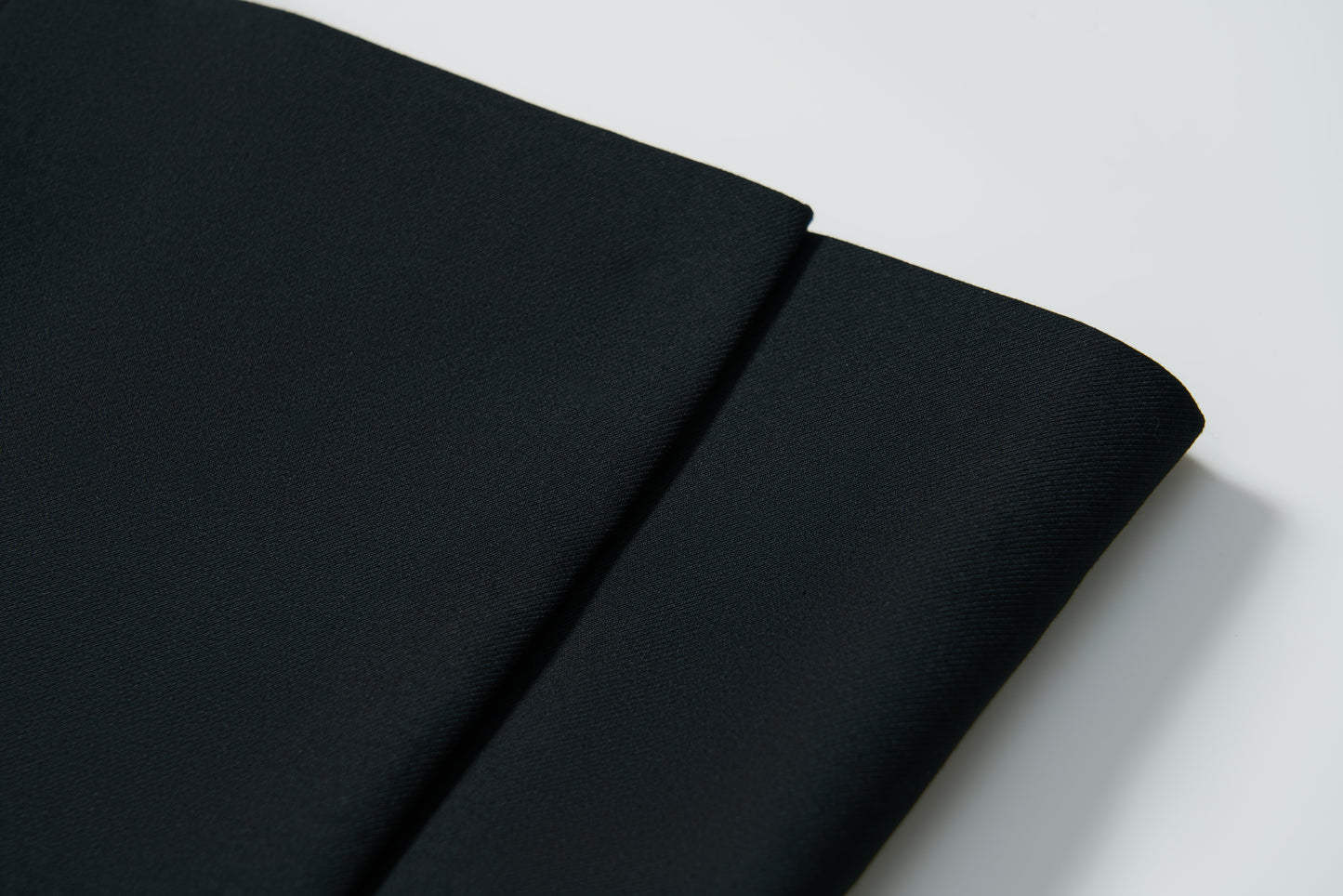 Close-up of two folded pieces of plain black fabric on a white surface—ideal for creating the KIKI and JOJO Noir Bloom Suit Jacket, a timeless choice for boys.