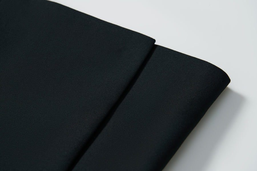 Close-up of two folded pieces of plain black fabric on a white surface—ideal for creating the KIKI and JOJO Noir Bloom Suit Jacket, a timeless choice for boys.