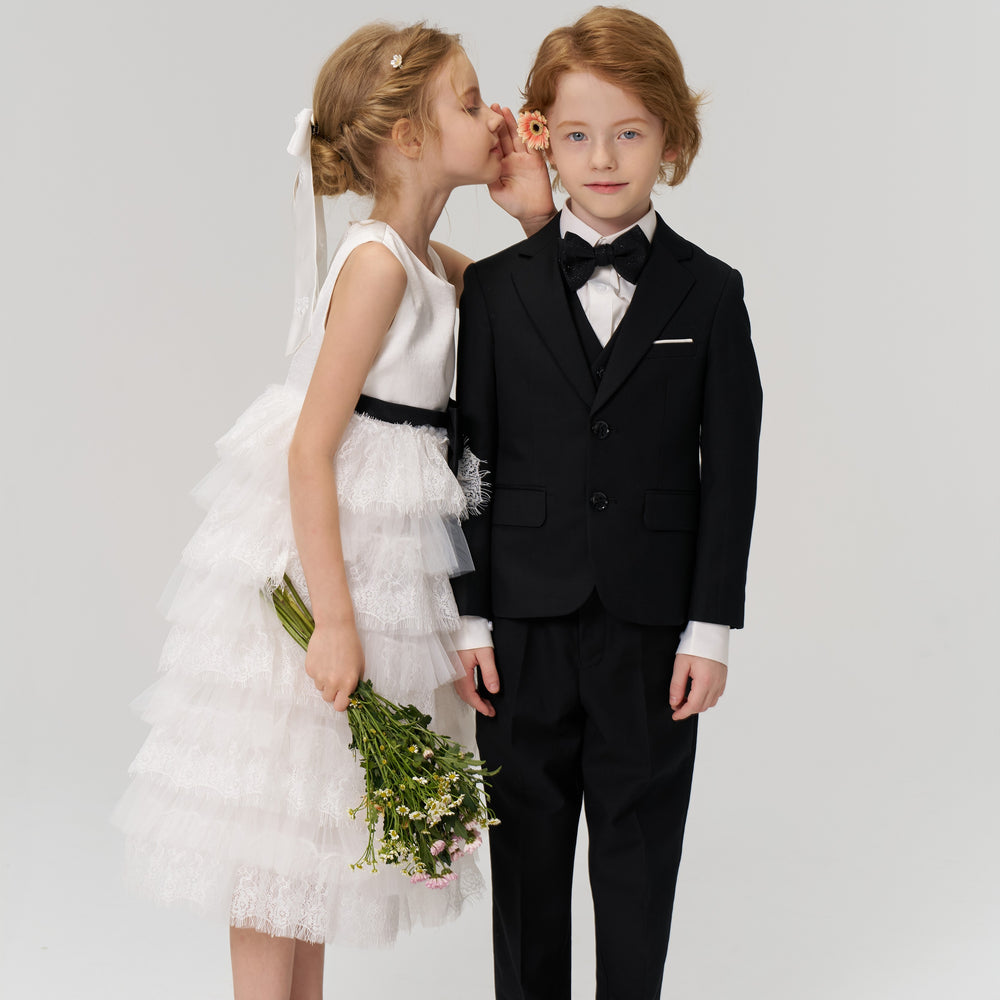 A girl whispering to a boy in a tuxedo.