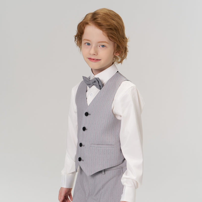 A young child with light brown hair wears a light gray suit, white dress shirt, and bow tie, standing against a plain light background.