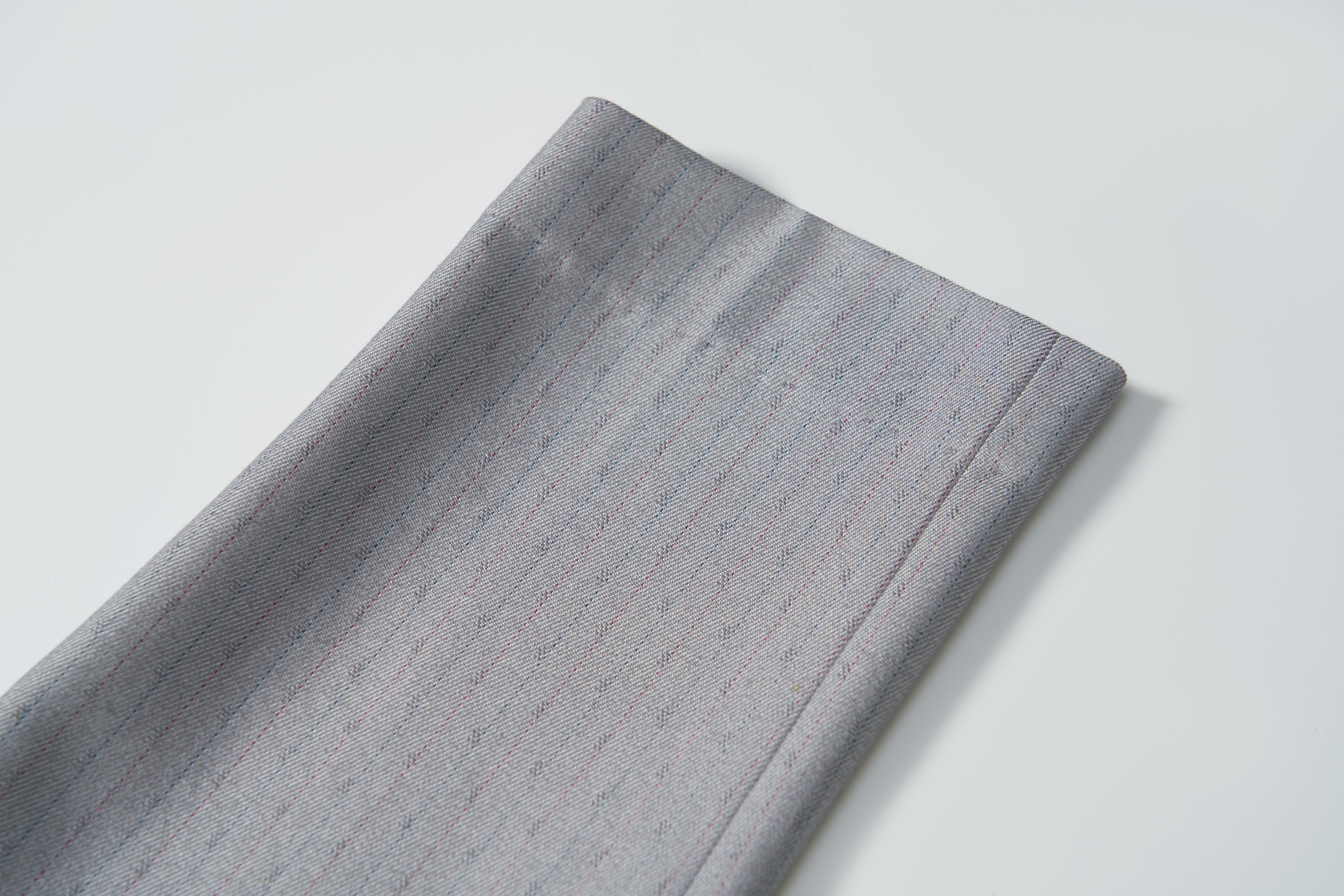 A close-up of Silver Bloom Suit Pants by KIKI and JOJO, showing folded gray fabric with subtle pinstripes—ideal for boys, featuring an adjustable waistband—displayed on a white background.