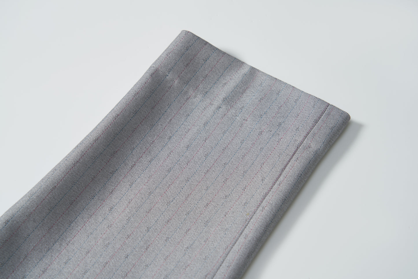 A close-up of Silver Bloom Suit Pants by KIKI and JOJO, showing folded gray fabric with subtle pinstripes—ideal for boys, featuring an adjustable waistband—displayed on a white background.