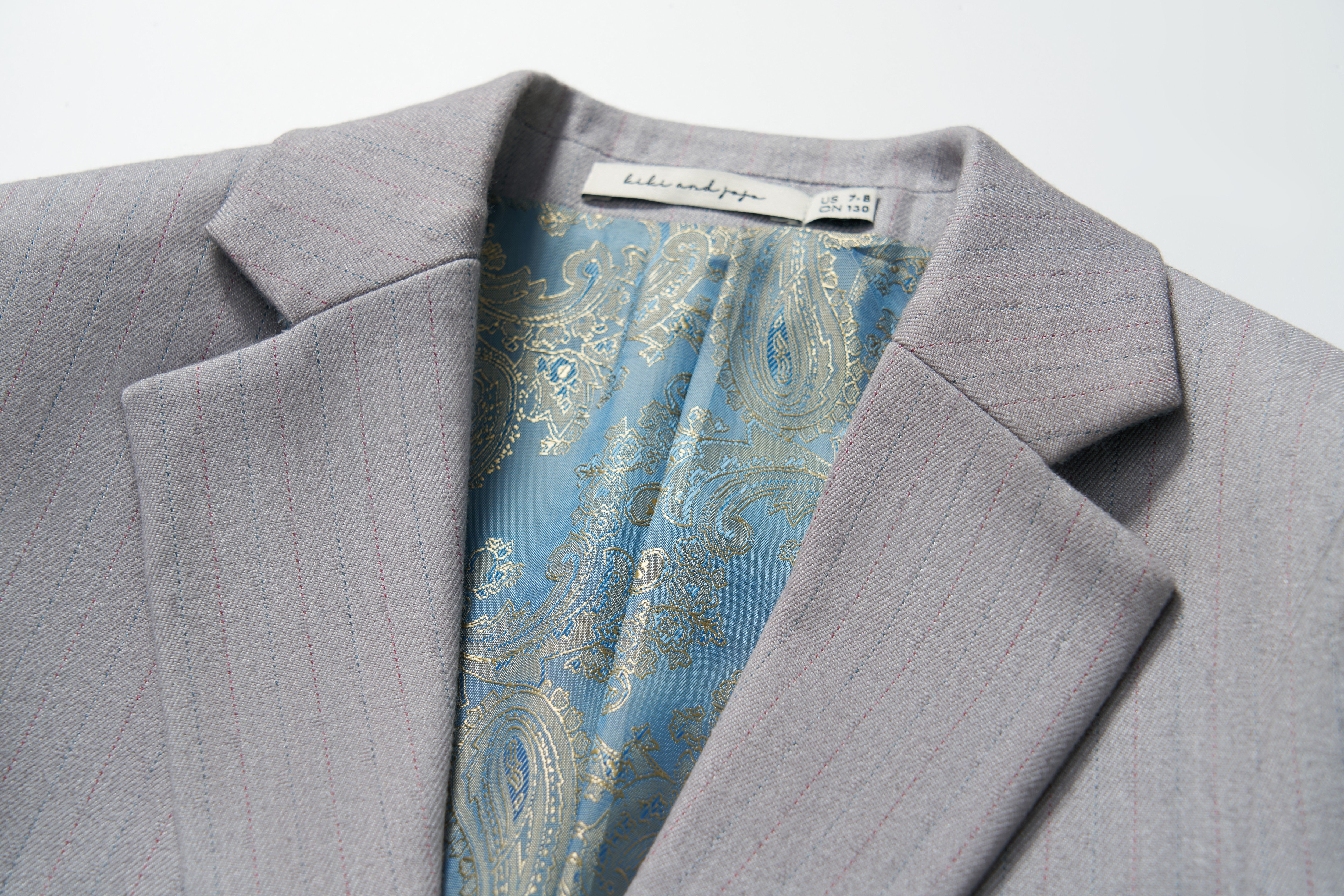 Close-up of the Silver Bloom Suit Jacket by KIKI and JOJO, featuring light gray stripes, a blue paisley inner lining, and a visible neck label—ideal for formal boys’ clothing.