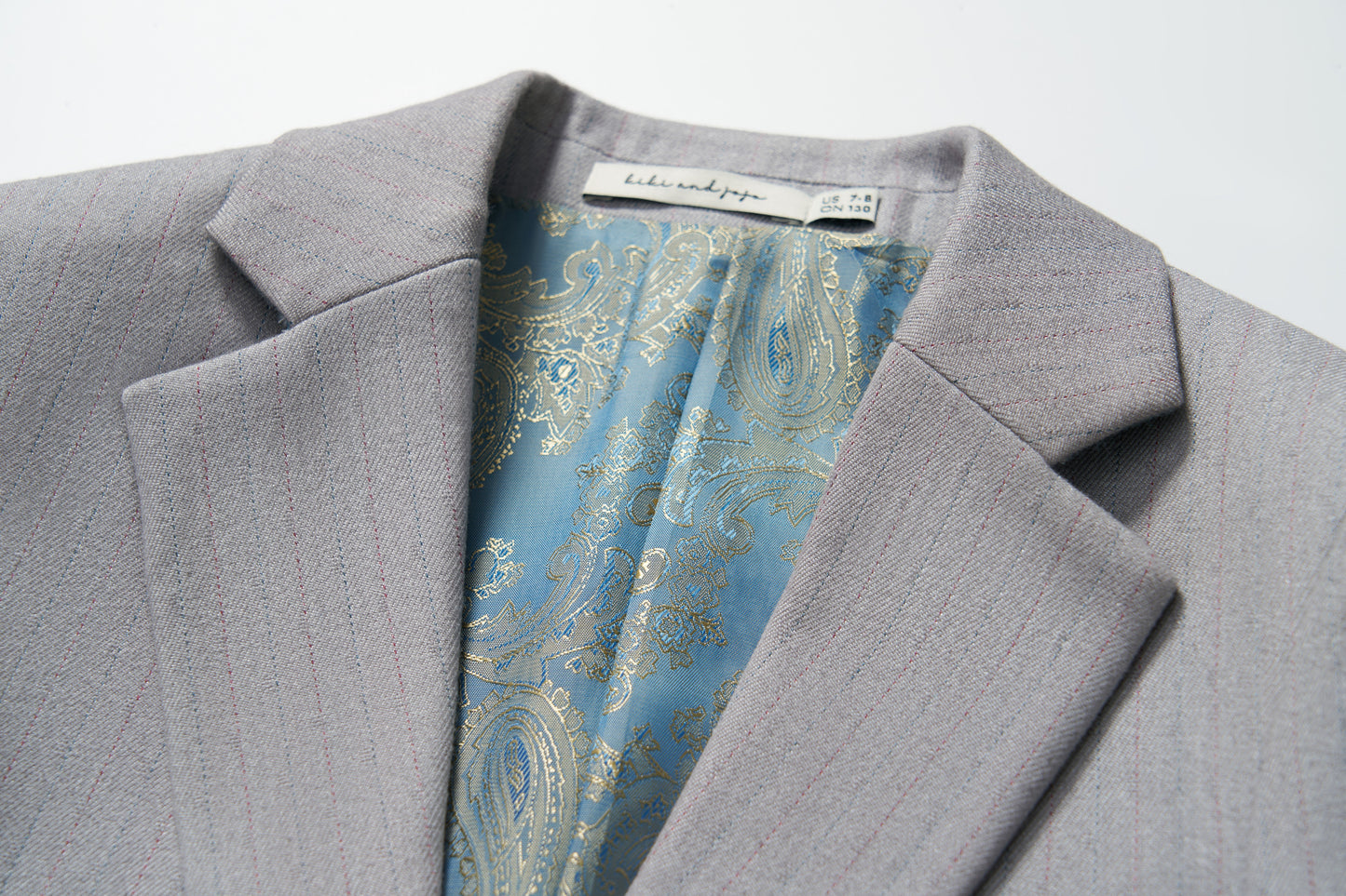 Close-up of the Silver Bloom Suit Jacket by KIKI and JOJO, featuring light gray stripes, a blue paisley inner lining, and a visible neck label—ideal for formal boys’ clothing.