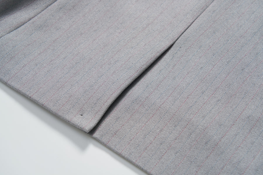 Close-up of the Silver Bloom Suit Jacket by KIKI and JOJO, showing its light gray pinstripe fabric with a seam and pleat, displayed on a white surface.