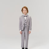 A young child with light brown hair wears the KIKI and JOJO Silver Bloom Suit Jacket, featuring light gray stripes, a bow tie, and black shoes against a plain studio background—ideal for formal boys’ occasions.