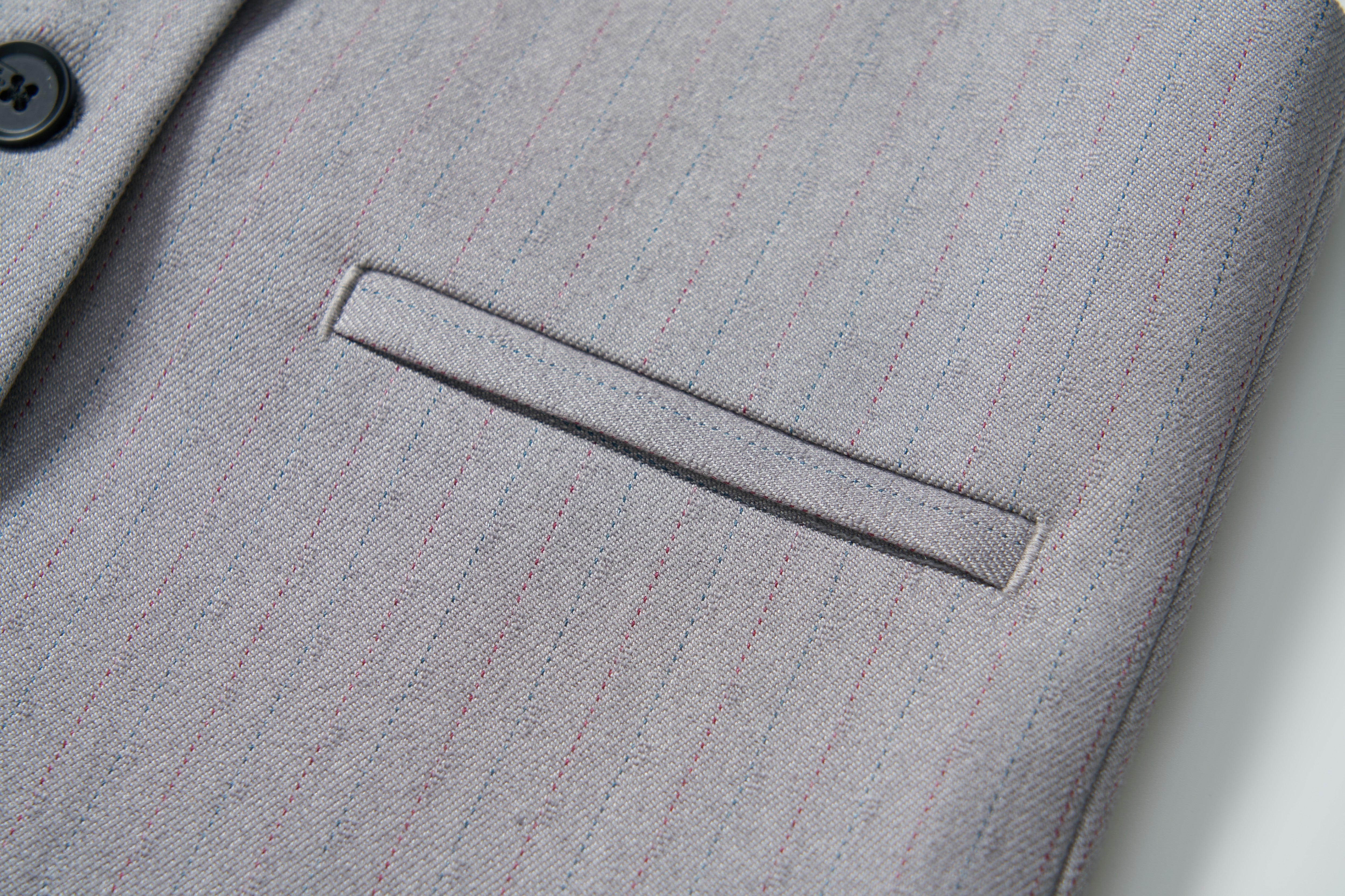 Close-up of a gray suit jacket with subtle pinstripes, welt pocket, and black button—ideal to pair with the KIKI and JOJO Silver Bloom Suit Vest for a refined look.