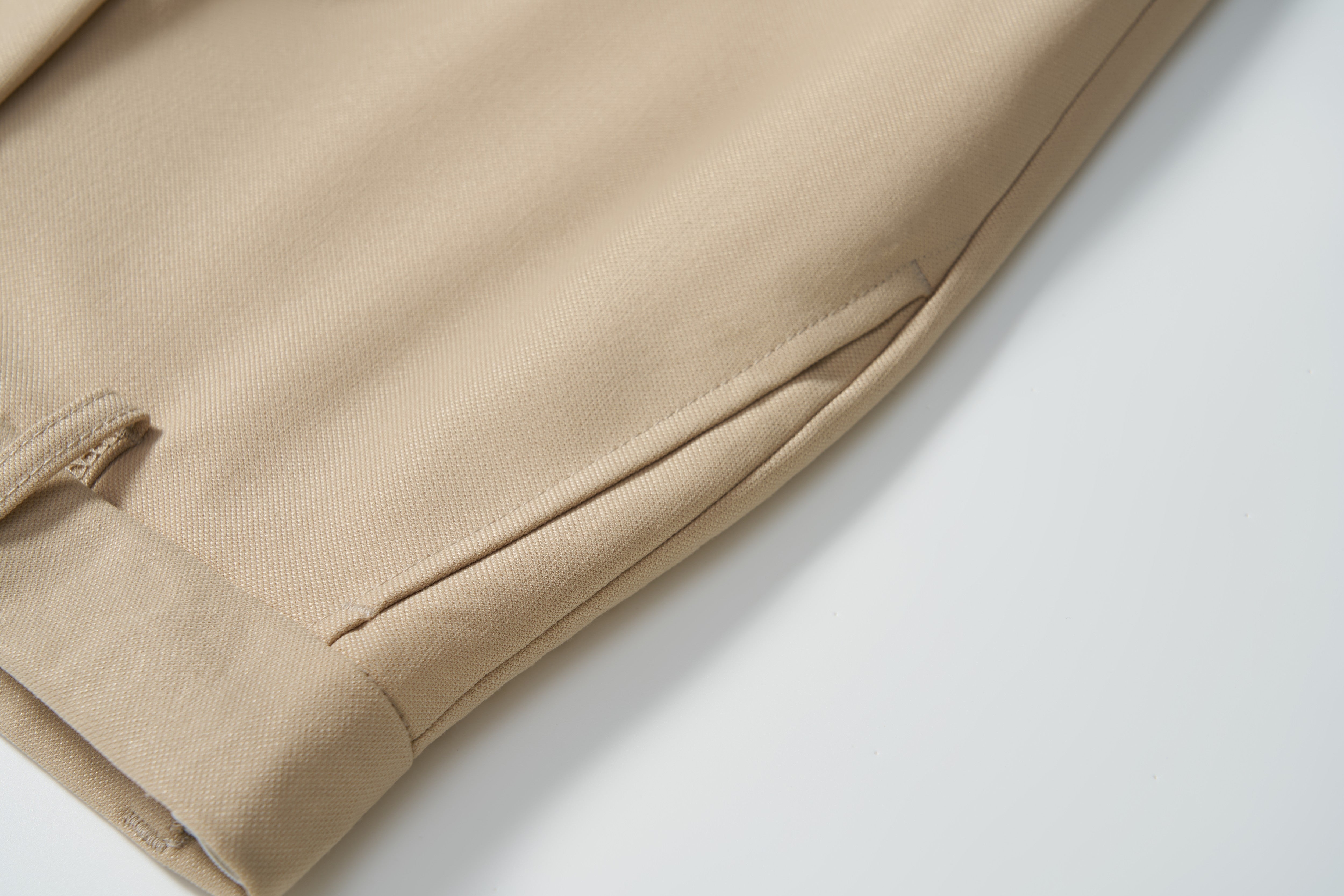 Close-up of the hem and side pocket of KIKI and JOJO Savoy Dune Suit Pants in beige, featuring detailed stitching, fabric texture, and an adjustable waistband against a white background.