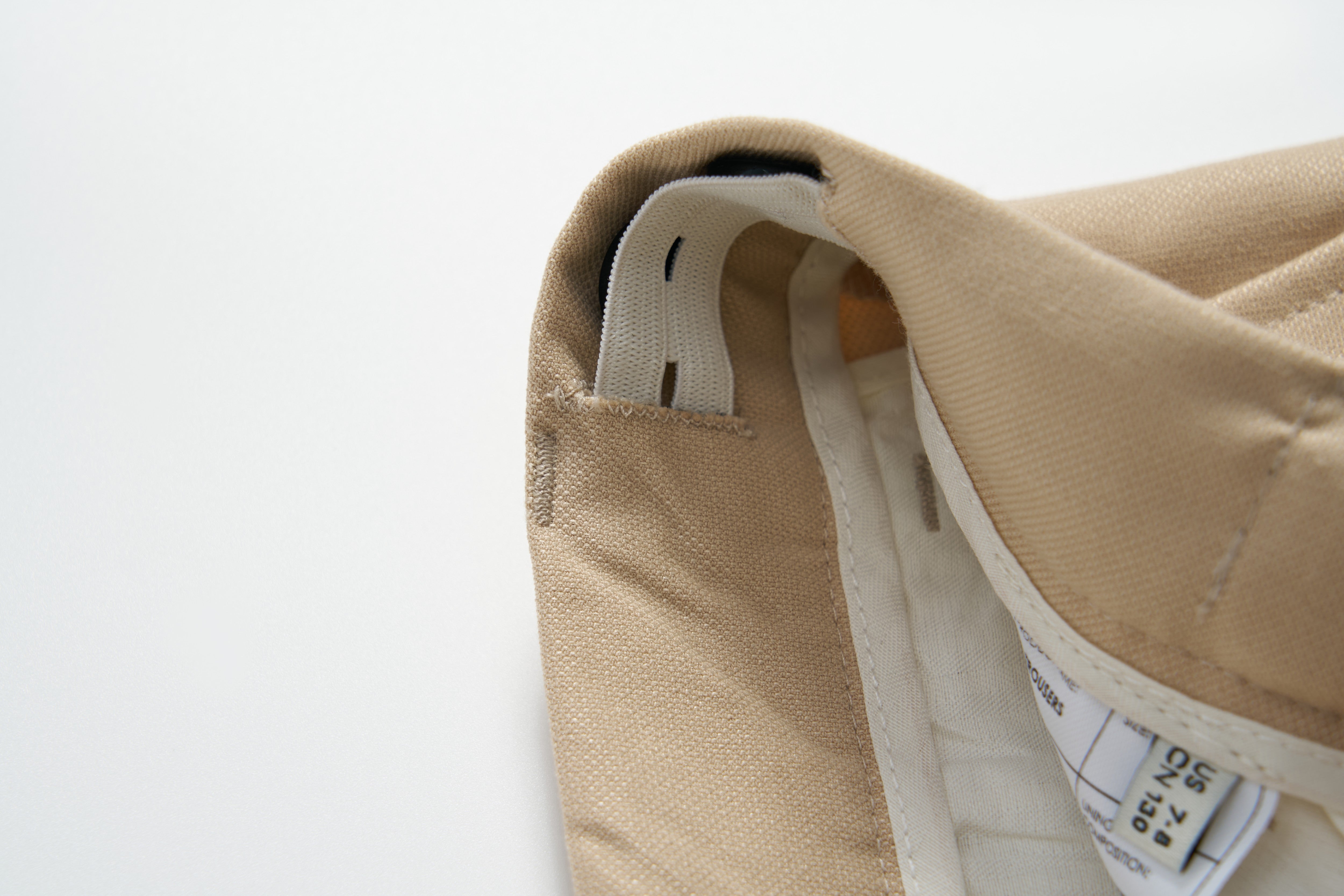 Close-up of the inside waistband of Savoy Dune Suit Pants by KIKI and JOJO, showing stitching, a fabric loop, an adjustable waistband, and a clothing label with care instructions.