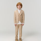 A young boy with red hair faces forward in KIKI and JOJO Savoy Dune Suit Pants with an adjustable waistband, paired with a white shirt and brown shoes, all set against a plain light background.
