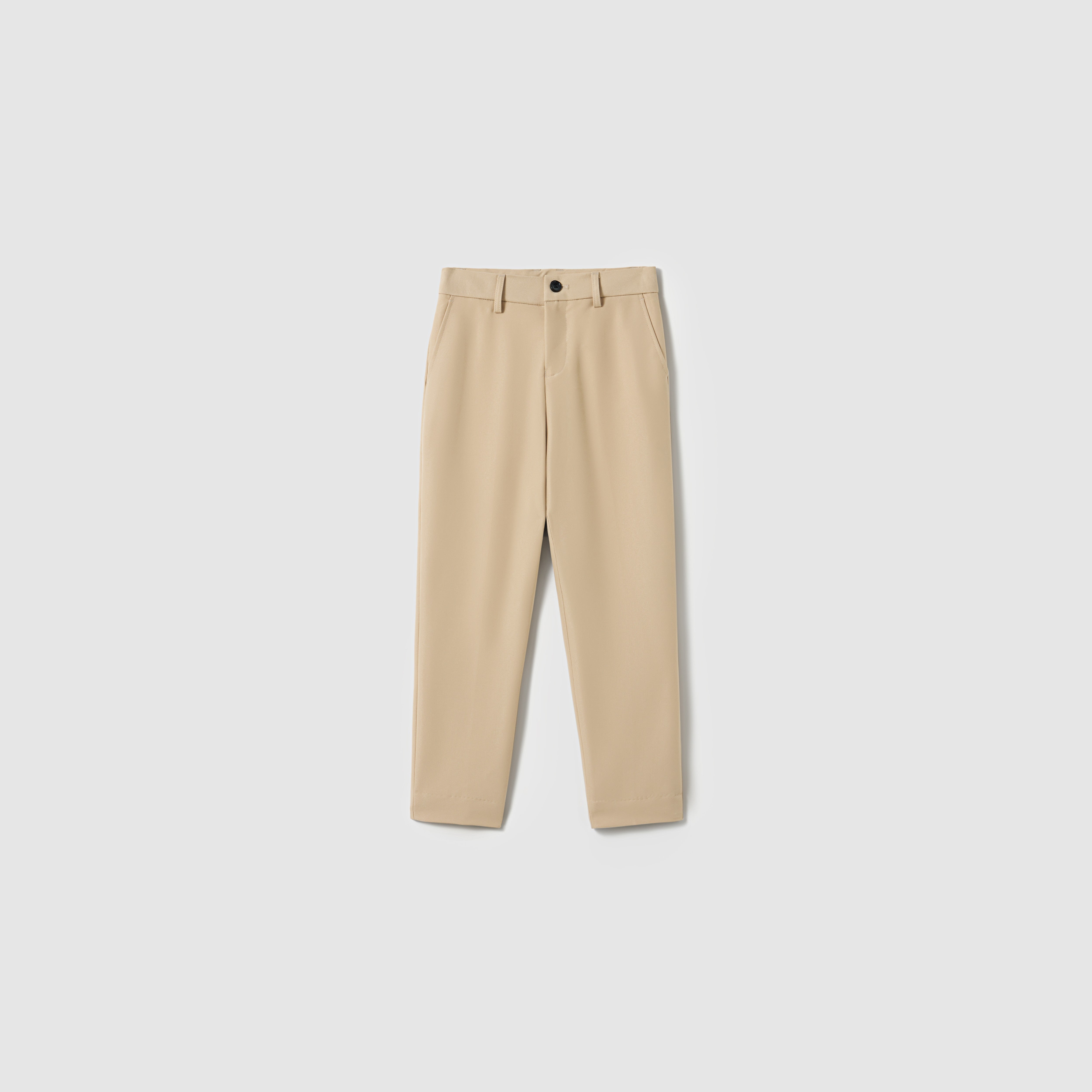 The Savoy Dune Suit Pants by KIKI and JOJO are beige boys' straight-leg dress pants with belt loops, side pockets, an adjustable waistband, and a front button closure, shown on a plain light gray background.