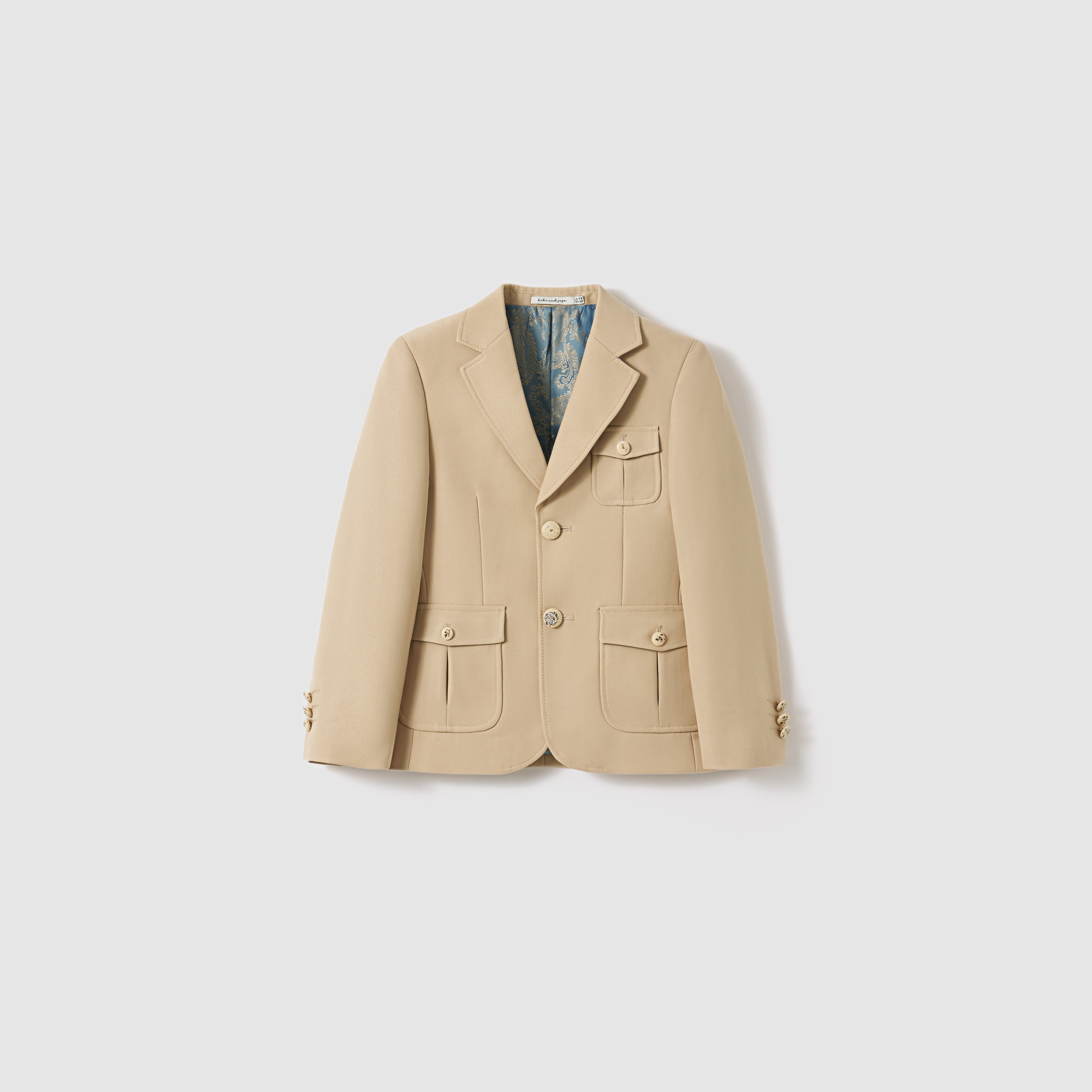 The Savoy Dune Suit Jacket by KIKI and JOJO is a beige, single-breasted boys suit jacket with notch lapels, three pockets, button cuffs, and patterned lining—ideal formalwear for boys. Shown on a plain white background.