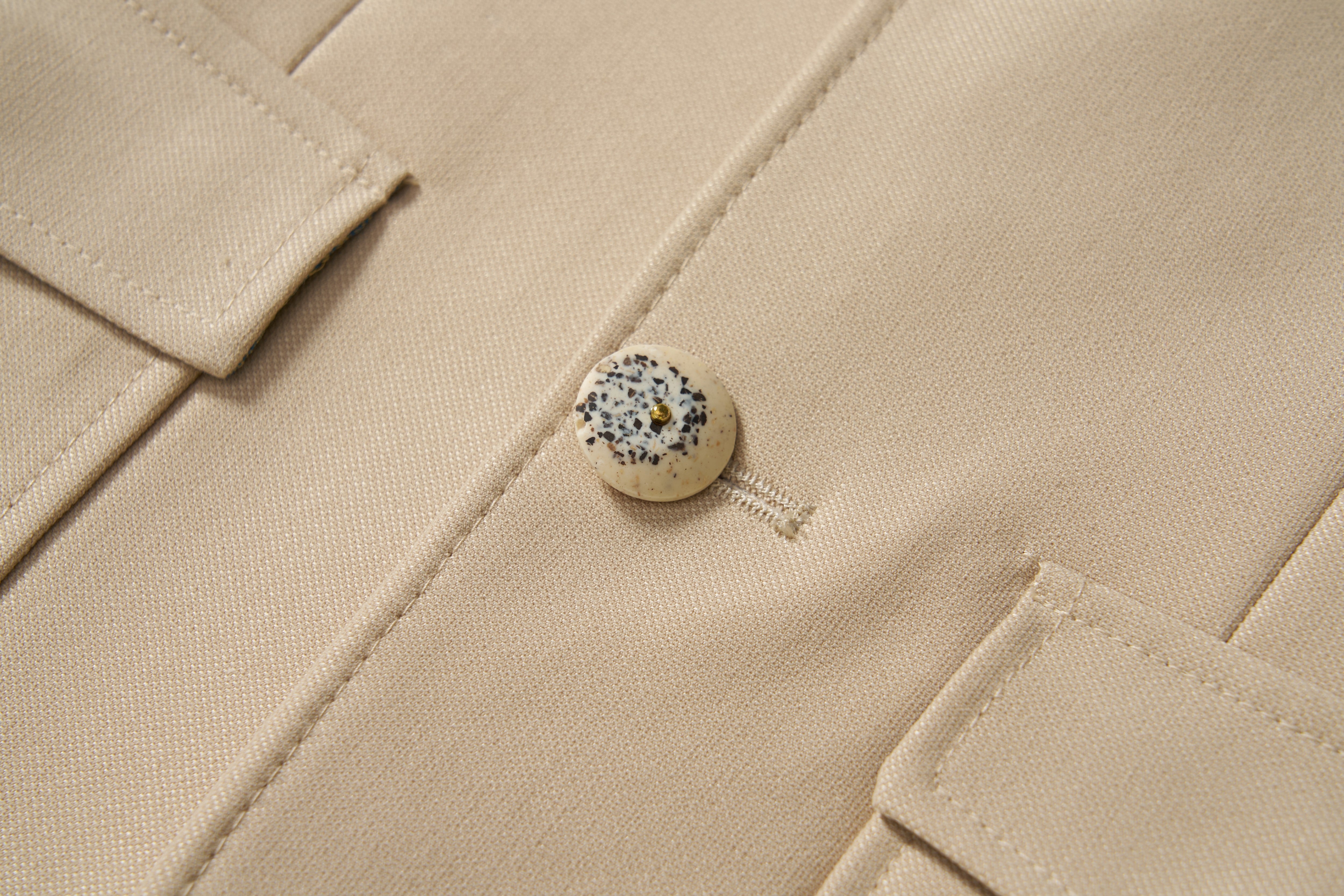 Close-up of the Savoy Dune Suit Jacket by KIKI and JOJO, a khaki boys piece in classic tailoring with a single speckled round button fastened and two flap pockets partially visible.
