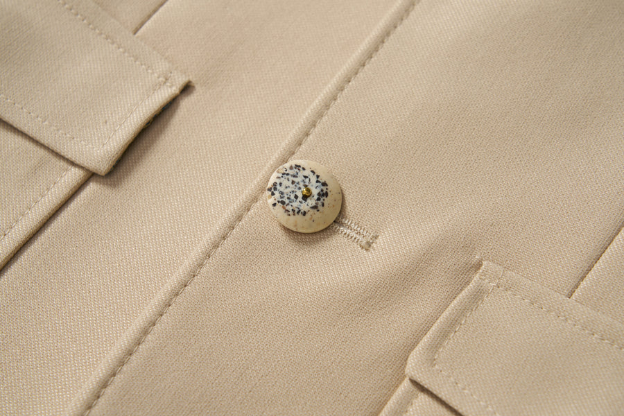 Close-up of the Savoy Dune Suit Jacket by KIKI and JOJO, a khaki boys piece in classic tailoring with a single speckled round button fastened and two flap pockets partially visible.