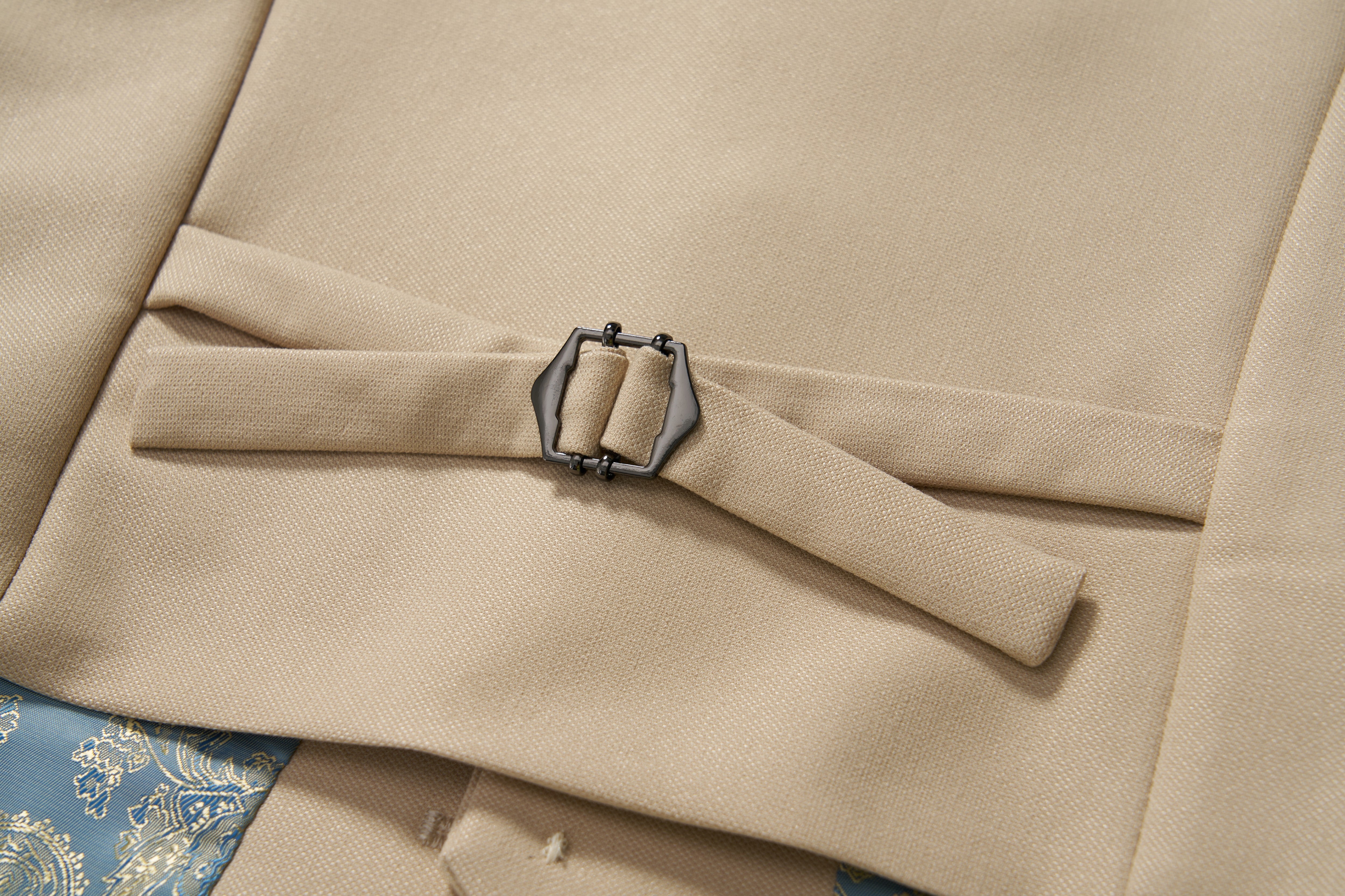 Close-up of a khaki beige suit jacket with a metal side adjuster and fabric strap, revealing part of the Savoy Dune Suit Vest by KIKI and JOJO in blue and gold pattern underneath.