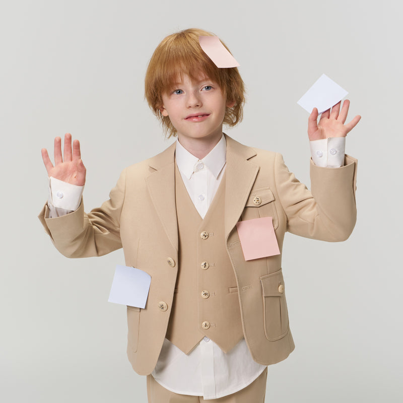 A young child in a beige suit stands with hands raised, covered in various pastel-colored sticky notes on their face, hands, and jacket.